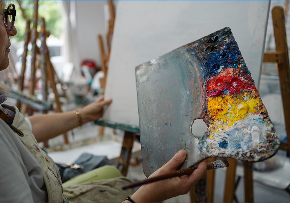 Senior woman artist holding a palette and painting on canvas
